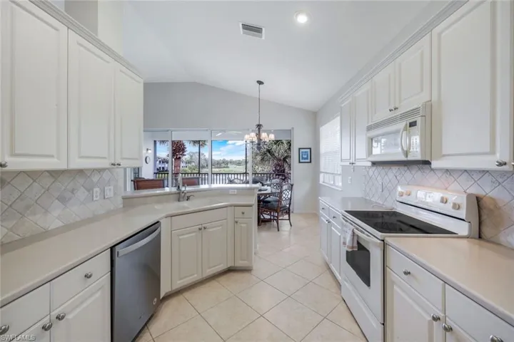 Kitchen featuring tasteful backsplash, white appliances, light countertops, a peninsula, and decorative light fixtures