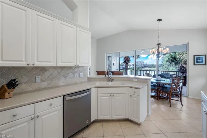 Kitchen with dishwasher, light countertops, a peninsula, a chandelier, and lofted ceiling