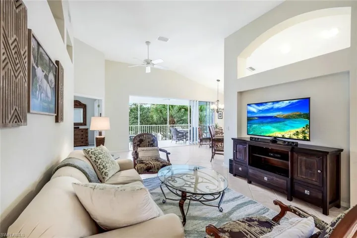 Living room featuring light tile patterned floors, ceiling fan, high vaulted ceiling, and a chandelier
