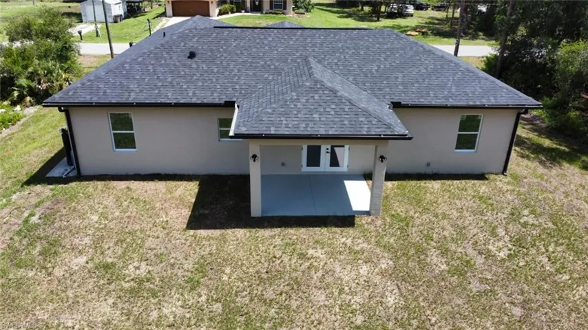 Back of property featuring a shingled roof, a patio area, stucco siding, and a lawn