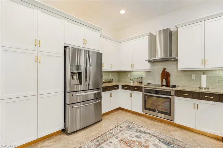 Kitchen with stainless steel appliances, white cabinets, wall chimney exhaust hood, backsplash, and light stone countertops