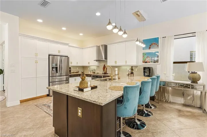 Kitchen with a kitchen breakfast bar, stainless steel refrigerator with ice dispenser, light stone counters, white cabinets, and hanging light fixtures