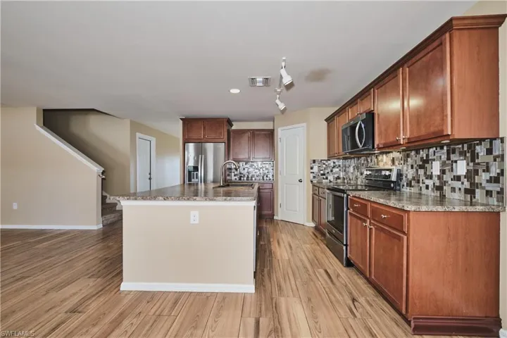 Kitchen with stainless steel appliances, an island with sink, decorative backsplash, light wood-type flooring, and dark stone countertops
