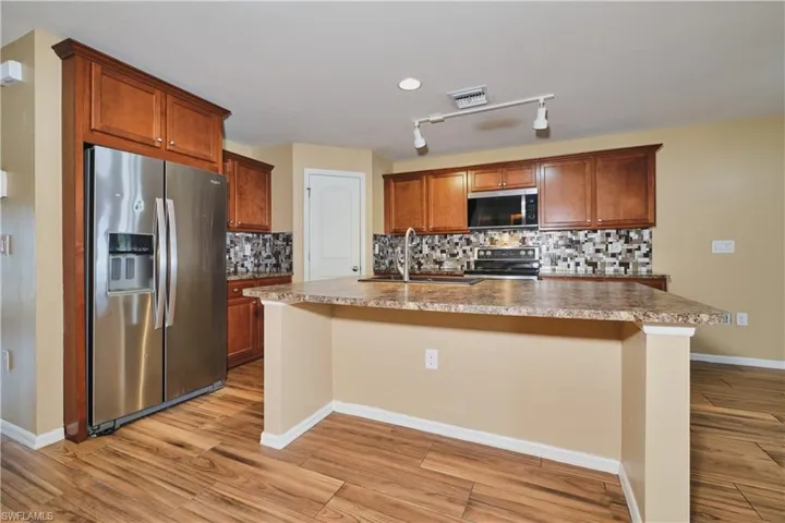 Kitchen featuring stainless steel appliances, decorative backsplash, a kitchen island with sink, light wood-type flooring, and wood finish cabinets