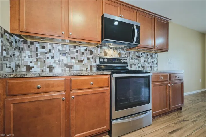 Kitchen with stainless steel appliances, wood finish cabinets, light wood finished floors, backsplash, and light stone countertops