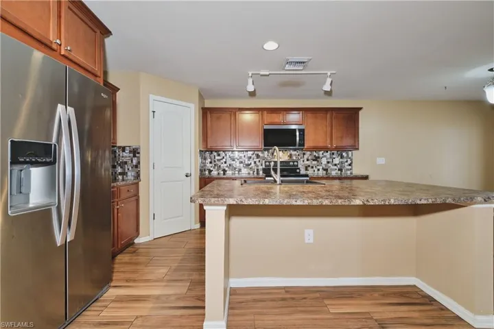 Kitchen featuring stainless steel appliances, backsplash, light wood-style flooring, wood finish cabinetry, and rail lighting