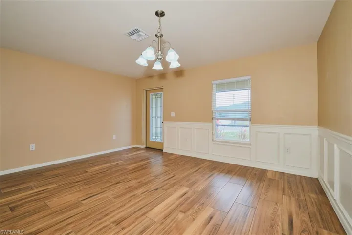 Empty room featuring hanging lights, a decorative wall, wainscoting, and light wood-style flooring