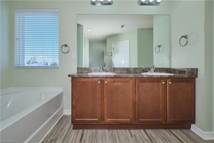 Full bath featuring double vanity, a garden tub, and light wood-style flooring