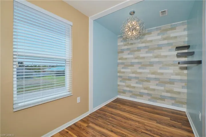 Unfurnished dining area with a chandelier, dark wood-type flooring, and an accent wall
