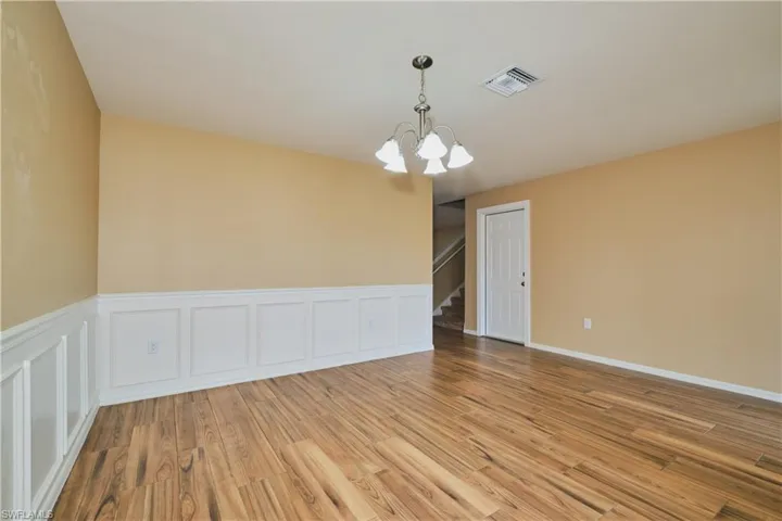 Empty room with hanging lights, a decorative wall, light wood-style floors, and a wainscoted wall