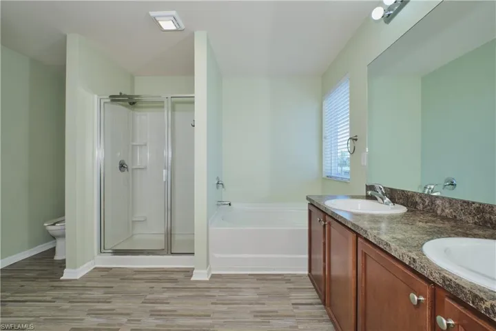 Bathroom with double vanity, a shower stall, a garden tub, and light wood-style floors