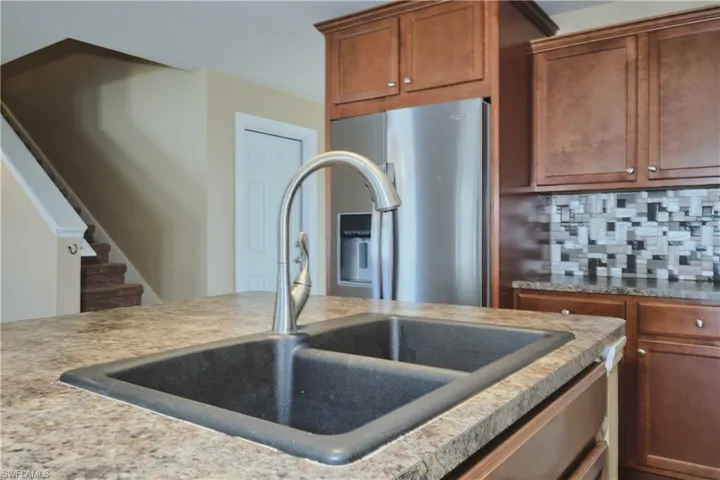 Kitchen featuring wood finish cabinets, stainless steel fridge, decorative backsplash, and light countertops