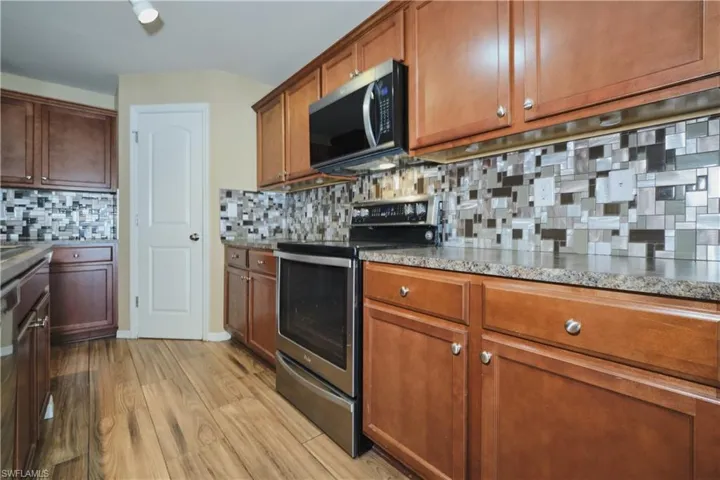 Kitchen featuring stainless steel range with electric stovetop, light wood-style floors, wood finish cabinets, decorative backsplash, and light stone countertops