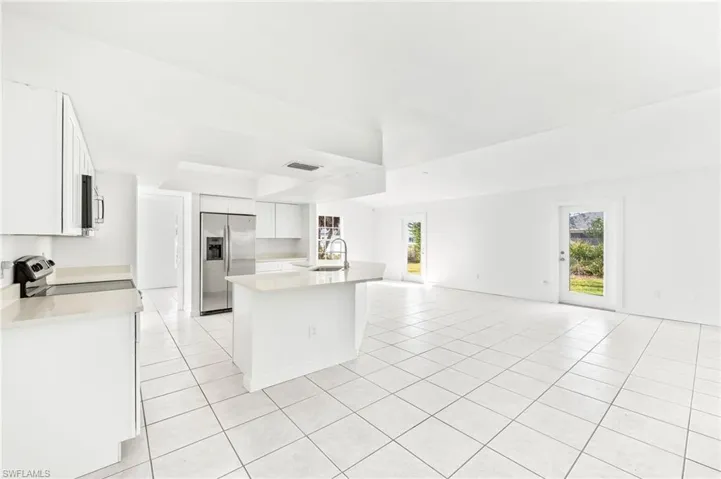 Kitchen featuring white cabinetry, a center island with sink, appliances with stainless steel finishes, and light tile patterned floors