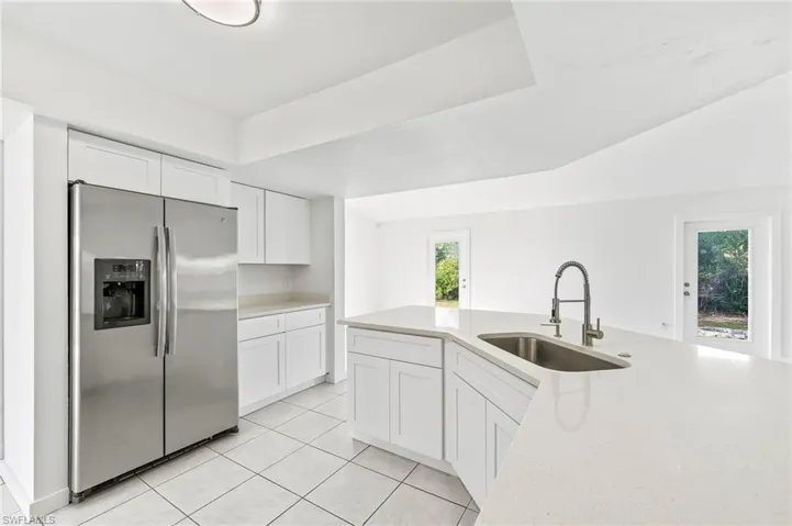 Kitchen with light tile patterned floors, white cabinets, quartz countertops, appliances & sink with stainless steel finishes.