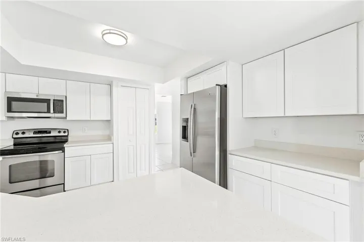 Kitchen with light tile patterned floors, white cabinets, quartz countertops, appliances & sink with stainless steel finishes.
