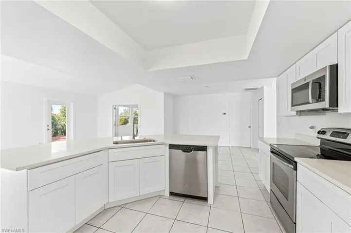 Kitchen with light tile patterned floors, white cabinets, quartz countertops, appliances & sink with stainless steel finishes.