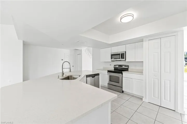 Kitchen with light tile patterned floors, white cabinets, quartz countertops, appliances & sink with stainless steel finishes.