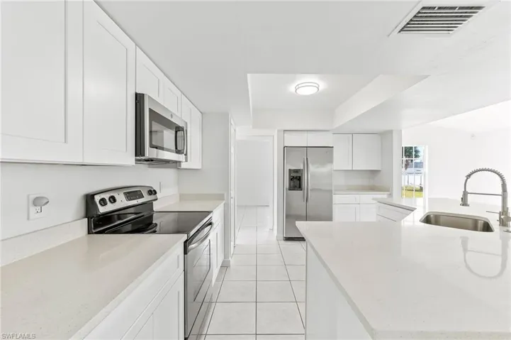 Kitchen with light tile patterned floors, white cabinets, quartz countertops, appliances & sink with stainless steel finishes.