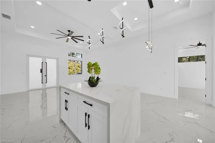 Kitchen with ceiling fan, open floor plan, white cabinets, and a tray ceiling