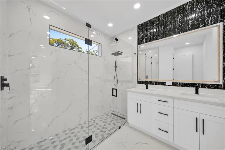 Bathroom with a marble finish shower, double vanity, recessed lighting, stone wall, and light marble finish floors