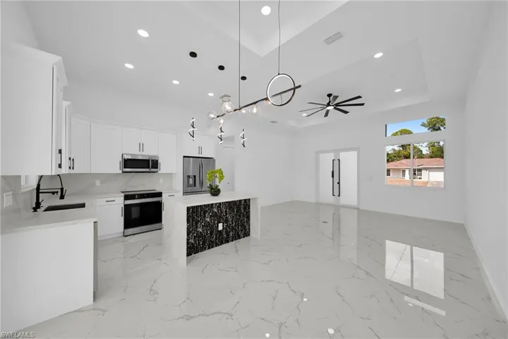 Kitchen featuring white cabinetry, open floor plan, light stone countertops, decorative light fixtures, and stainless steel appliances