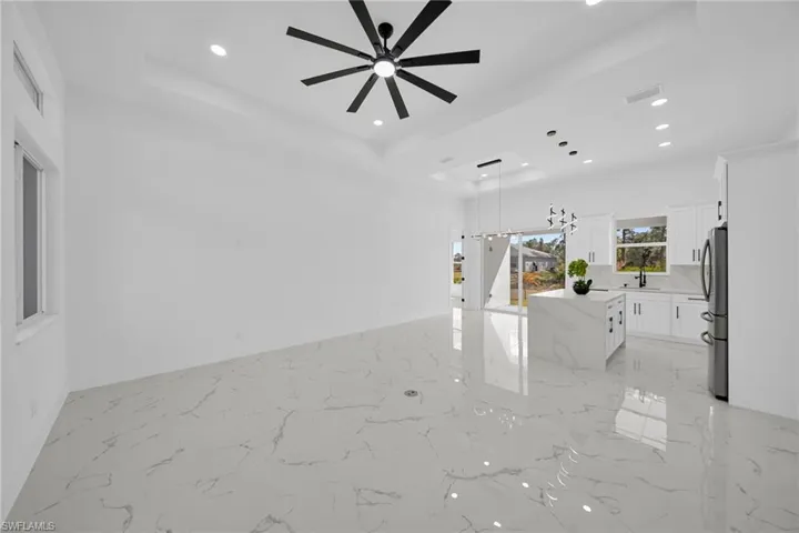 Unfurnished living room with a ceiling fan, recessed lighting, light marble finish flooring, and a raised ceiling