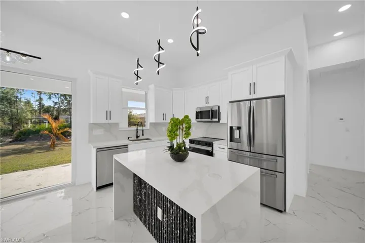 Kitchen with a kitchen island, stainless steel appliances, white cabinetry, light stone counters, and decorative backsplash