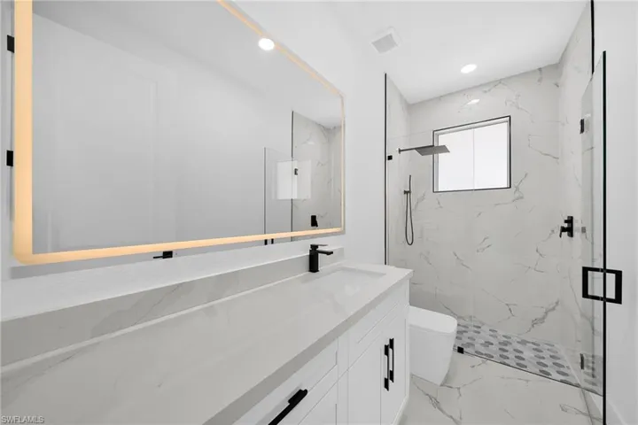 Bathroom with a marble finish shower, vanity, recessed lighting, and light marble finish flooring