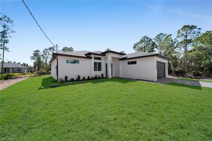 Prairie-style house with a front yard, stucco siding, driveway, roof with shingles, and an attached garage