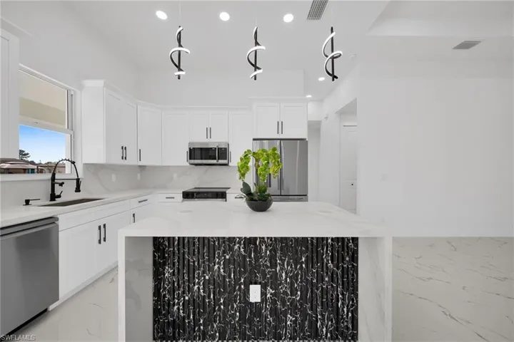 Kitchen featuring light stone counters, stainless steel appliances, white cabinetry, a kitchen island, and tasteful backsplash