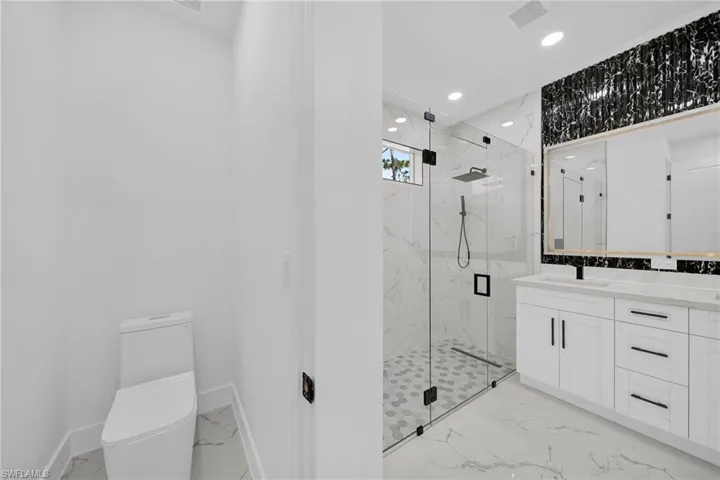 Full bath with light marble finish flooring, vanity, a marble finish shower, and recessed lighting