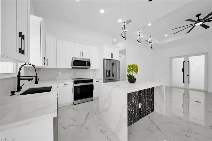 Kitchen with stainless steel appliances, light stone counters, hanging light fixtures, white cabinetry, and backsplash