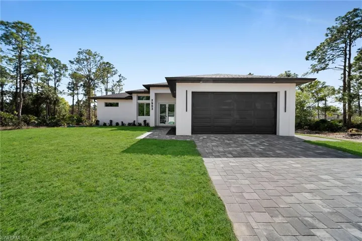 Prairie-style house with decorative driveway, a front lawn, an attached garage, and stucco siding