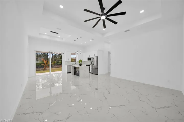 Unfurnished living room featuring light marble finish floors, a raised ceiling, hanging lights, and ceiling fan