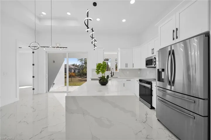 Kitchen featuring stainless steel appliances, white cabinetry, light stone countertops, light marble finish floors, and decorative light fixtures