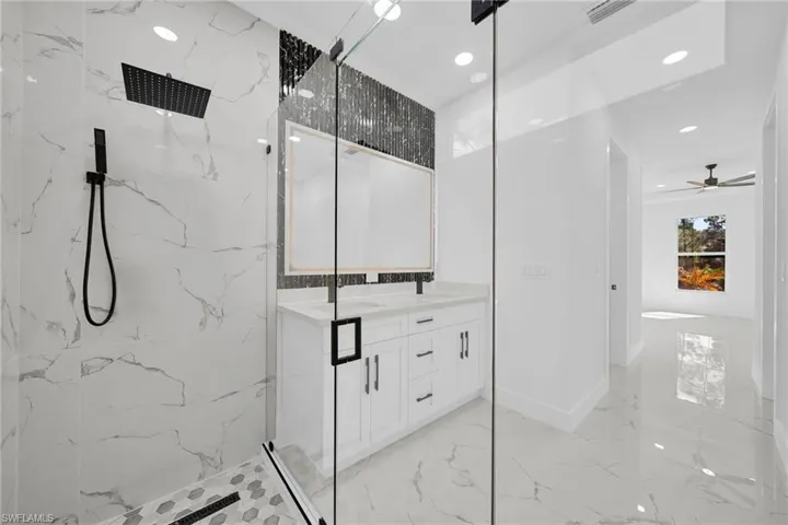 Bathroom featuring a marble finish shower, double vanity, light marble finish flooring, recessed lighting, and ceiling fan