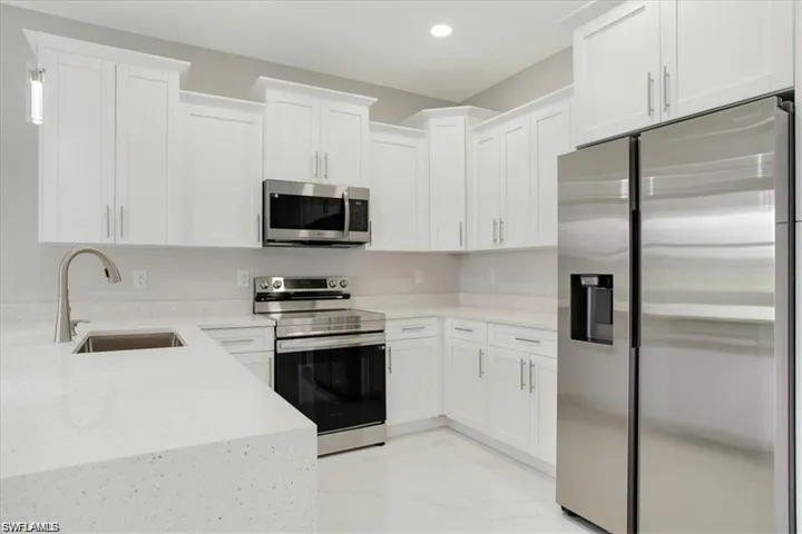 Kitchen featuring stainless steel appliances, white cabinetry, sink, and light stone counters