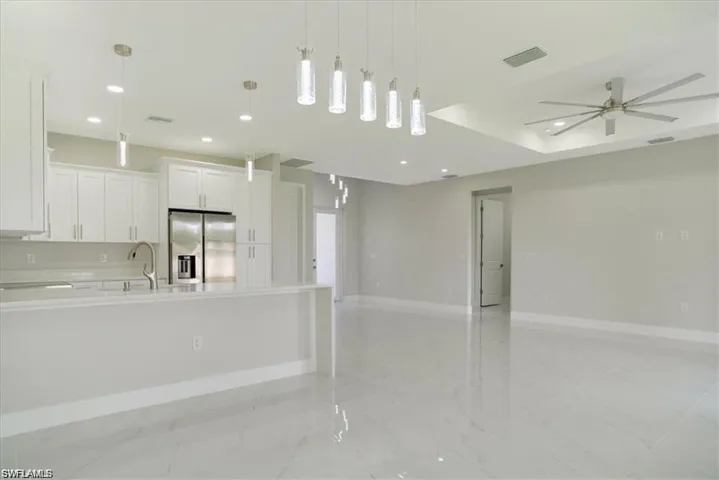 Kitchen with white cabinetry, ceiling fan, hanging light fixtures, stainless steel fridge, and a kitchen island with sink