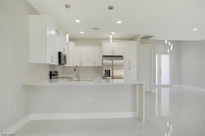 Kitchen featuring kitchen peninsula, hanging light fixtures, stainless steel appliances, white cabinets, and sink