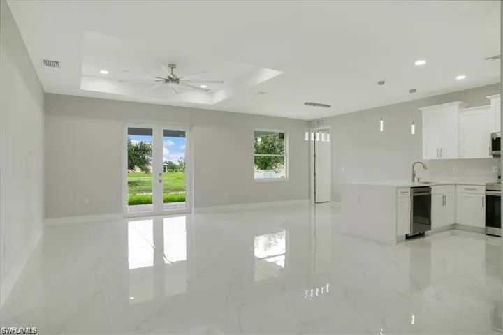 Unfurnished living room featuring ceiling fan, french doors, sink, and a tray ceiling
