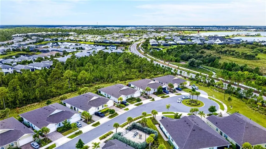 Aerial perspective of a residential community featuring single-story homes with dark shingle roofs, a landscaped cul-de-sac with a central island, and proximity to expansive natural areas
