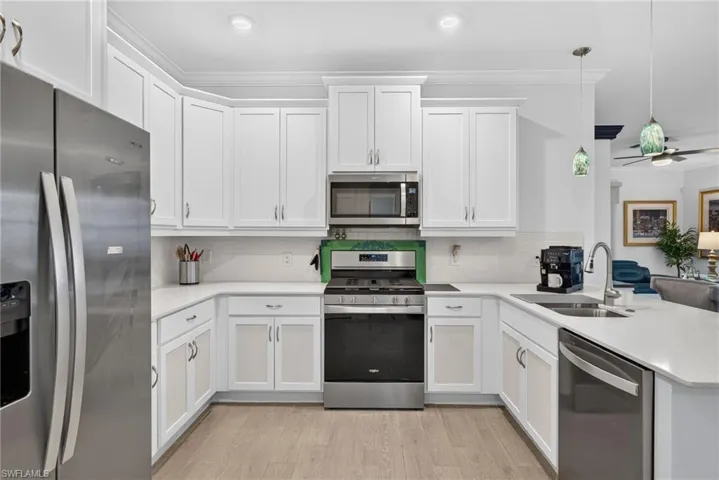 U-shaped kitchen featuring white cabinetry, stainless steel appliances, a white tile backsplash, and light wood-finish flooring
