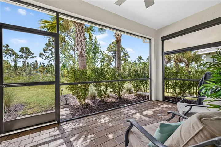 Screened-in patio with brick paver flooring, overhead ceiling fan, and lush landscaping