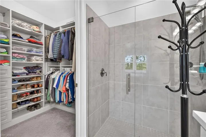 Custom built-in closet shelving, integrated hanging rods, walk-in shower with clear glass enclosure, tiled shower walls, and a tiled shower pan