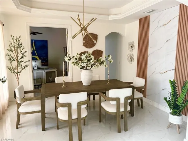 Dining space featuring light marble finish flooring, a tray ceiling, and arched walkways