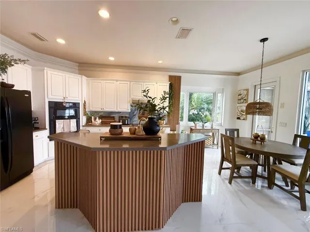 Kitchen with dark countertops, black appliances, a kitchen island, crown molding, and white cabinetry