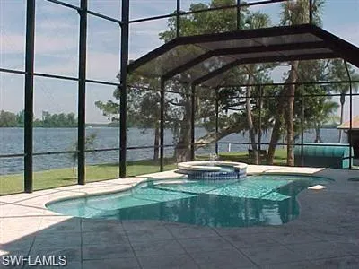 View of swimming pool featuring glass enclosure, a pool with connected hot tub, a sunroom, a water view, and a patio