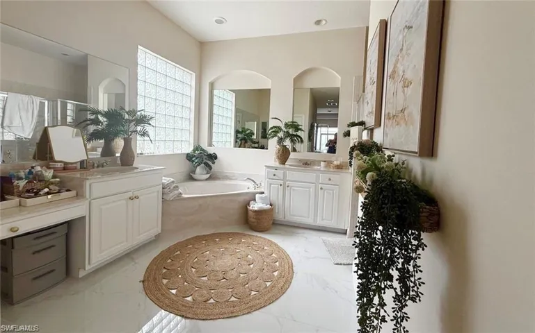 Bathroom with a bath, plenty of natural light, two vanities, and light marble finish floors