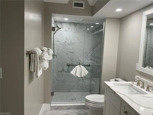 Bathroom featuring light marble finish flooring, a marble finish shower, and vanity